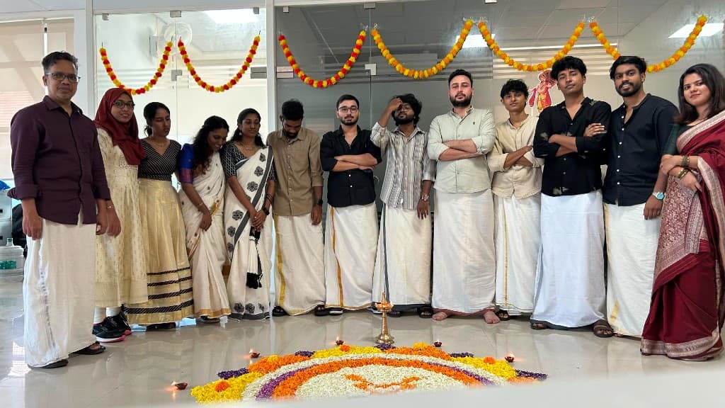 Team in traditional attire posing behind an Onam pookalam in the office
